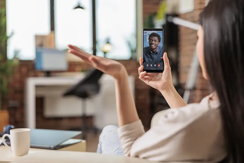 Woman video calling a recruiter from PrideStaff Dallas on her smartphone from a home office.
