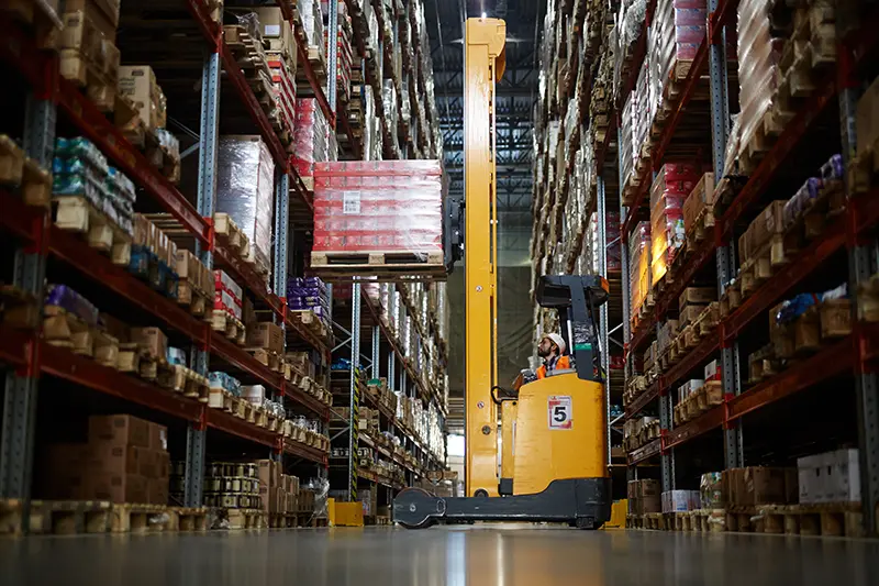 Stand-up reach truck operator placing a pallet on upper shelving in a Dallas warehouse