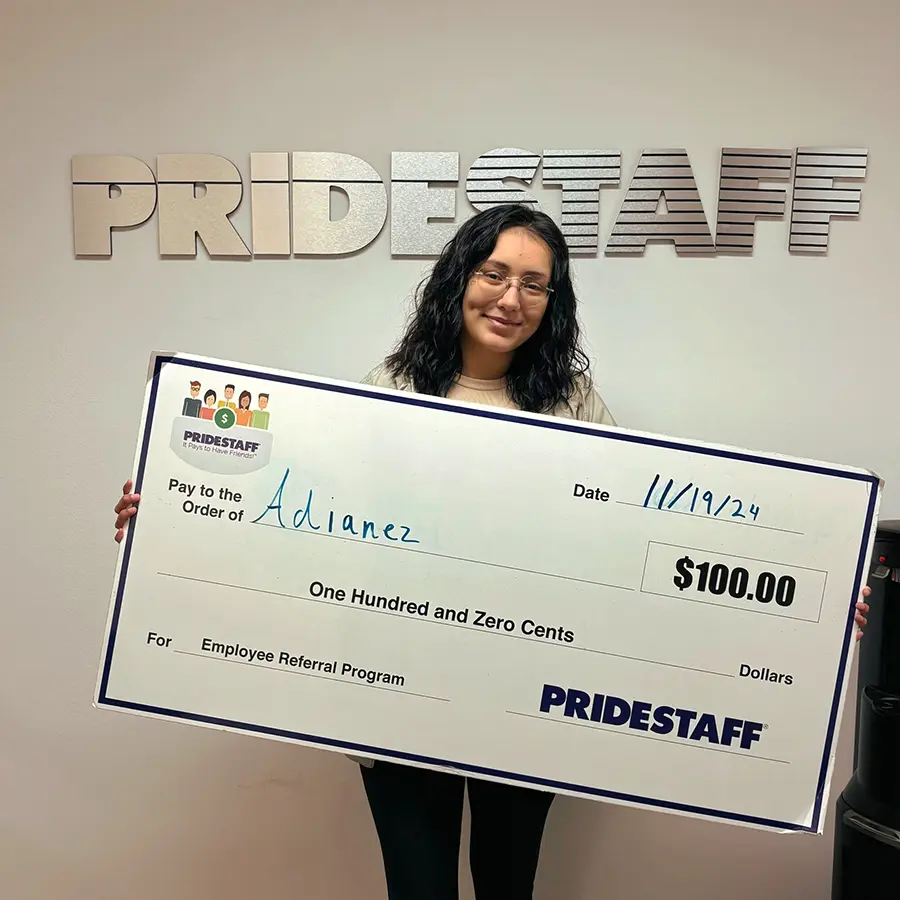 Adianez holding a $100 check from PrideStaff Dallas earned through the It Pays to Have Friends employee referral program.